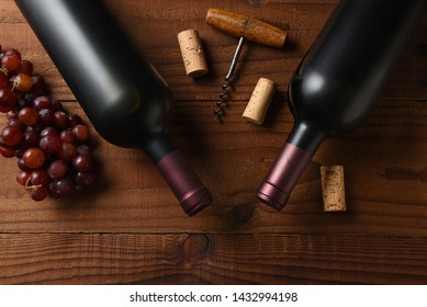 Wine Still Life: Two Cabernet Sauvignon Wine Bottle Short From Directly Above On A Dark Wood Table With Grapes Corks And Cork Screw And Copy Space.