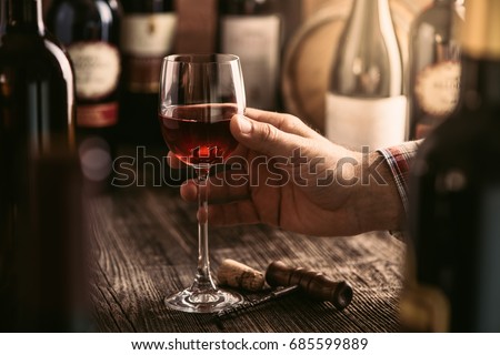 Wine tasting experience in the rustic cellar and wine bar: sommelier holding a glass of delicious red wine and excellent wine bottles collection on the background Zdjęcia stock © 