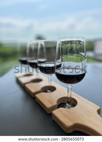 A wine tasting flight featuring red wines served on a wooden paddle at a winery in Niagara-on-the-Lake, Ontario, Canada. Captured with a shallow depth of field, the image highlights elegant glasses against a softly blurred vineyard backdrop, creating a refined atmosphere that celebrates tourism and vineyard experiences. Located in one of Canada’s most renowned wine regions, this photograph is ideal for themes of wineries, viticulture, hospitality, food and beverage, luxury travel, wine tasting, and culinary tourism. Perfect for winery marketing, travel guides, restaurant promotions, magazines, blogs, tourism campaigns, and lifestyle publications.