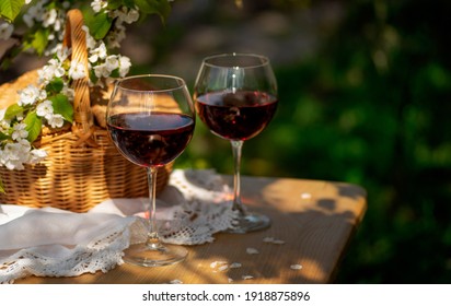 Wine Tasting Party In Spring In The Garden. Still Life With Long Stem Glasses With Red Wine On A Wooden Outdoor Table On The Beautiful Springtime Day. Blooming Branches With Cherry Flowers.
