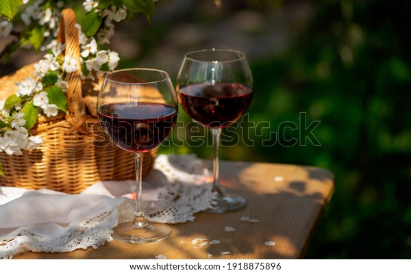 Wine Tasting Party in spring in the garden.\
Still life with long stem glasses with red wine on a wooden outdoor\
table on the beautiful springtime day. Blooming branches with\
cherry flowers.\
