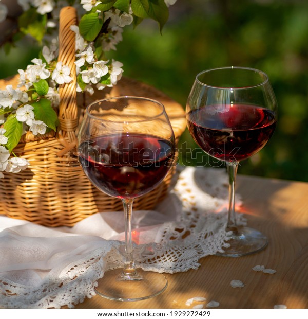 Wine Tasting Party in spring in the garden. Still\
life with long stem glasses with red wine on a wooden outdoor table\
on the beautiful springtime day. Blooming branches with cherry\
flowers