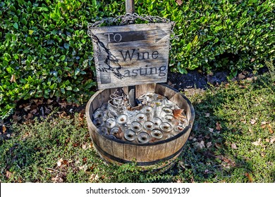 To wine tasting sign, with inverted glass bottles in a old wine cask / barrel and green foliage in the background.