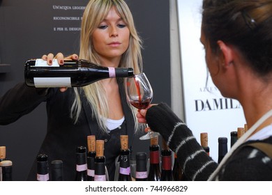 Wine trading fair people taste a wide selection of italian wines blonde woman puring red wine from bottle to glass Turin Italy circa November 2016