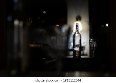 Wineglass And A Bottle Of Wine Stand On The Table In A Dark Room. Alcohol Abuse Concept. Abstract, Defocused Photo.