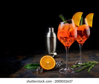 Wineglass of ice cold Aperol spritz cocktail served in a wine glass, decorated with slices of orange and rosemary branch. Black background. Copy space