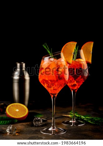 Wineglass of ice cold Aperol spritz cocktail served in a wine glass, decorated with slices of orange and rosemary branch. Black background. Copy space