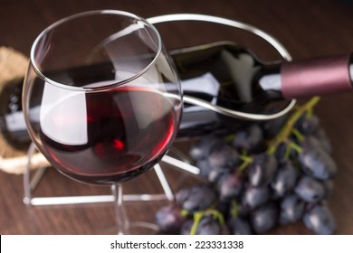 Wineglass with red wine with grapes and bottle at background