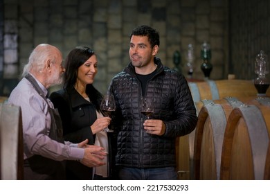 The Winemaker Guiding And Hosting A Young Caucasian Couple On The Tour Of The Wine Cellar, A Winery With A Long Production Tradition