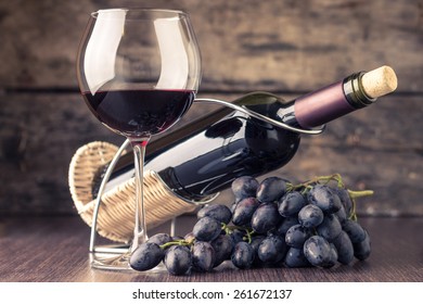 Winery background. Wineglass with bottle of red wine and cluster of grape on wooden table. Toned image
