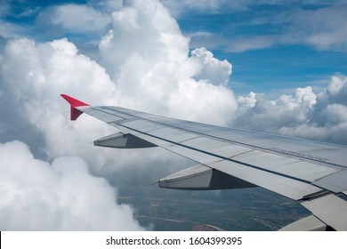 Wing of an airplane flying above the clouds on a clear sunny day. Aircraft flying high through the cumulus clouds.