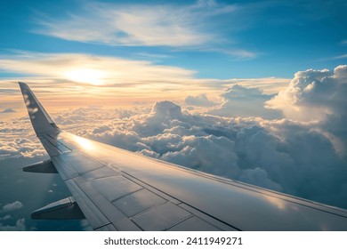 Wing of an airplane flying through the clouds at sunset and it is surrounded by fluffy white clouds. The sun is setting behind the clouds, casting a golden glow on the sky. - Powered by Shutterstock