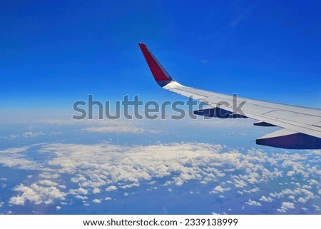 a wing of flying transportation jet plane with a red winglet in deep blue transparent sky background and a cloudy atmosphere below