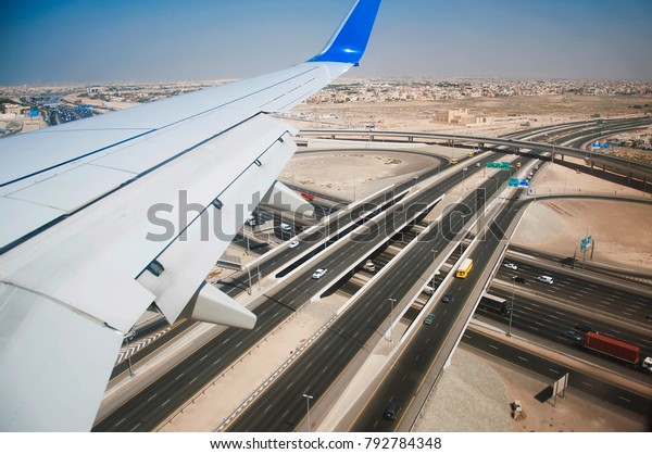 The wing of a low\
flying jet flying over the intersection of two highways in a\
deserted suburb of Dubai.