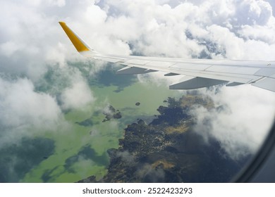 Wing of a passenger plane flying over Lake Skadar in Montenegro. Breathtaking view from the plane window through a gap in the clouds to the picturesque green lake, islands and winding coastline.