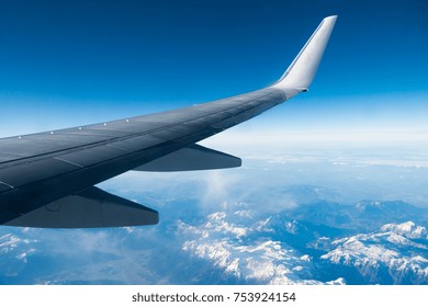 Wing of plane flying over clouds and mountains