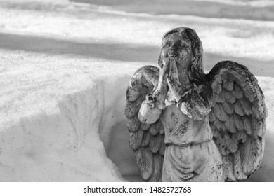 Winged Angel Praying And Partially Buried In Melting Snow Drift