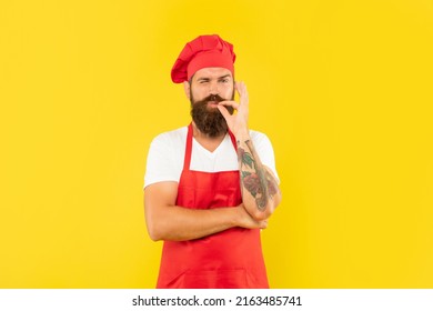 Winking Man In Red Apron And Toque Licking Finger Yellow Background, Chef