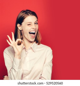 Winking Pretty Girl Young Beautiful Cute Woman Female Model With Red Hair In White Shirt Shows Ok Gesture Copy Space On Pink Background