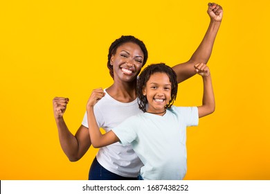 Winner Concept. Cheerful African Woman And Child Shaking Fists For Victory Isolated On Yellow Wall, Copyspace