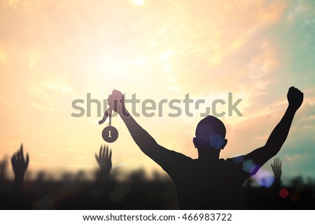 Winner concept: Silhouette champion hand holding gold medal reward against blurred sport stadium golden autumn sunset background