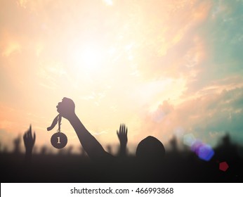 Winner concept: Silhouette human hand holding gold medal against twilight sky sunset background - Shutterstock ID 466993868