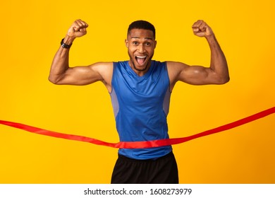 Winner. Excited Black Sportsman Running, Crossing The Finish Line Breaking The Tape, Yellow Studio Background