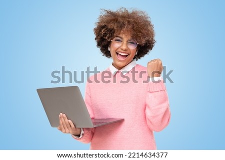 Winner! Excited smiling african girl with laptop, raising one hand in the air is she wins, isolated on blue background