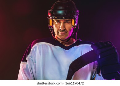 Winner. Male hockey player with the stick on ice court and dark neon colored background. Sportsman wearing equipment, helmet practicing. Concept of sport, healthy lifestyle, motion, wellness, action. - Shutterstock ID 1661190472