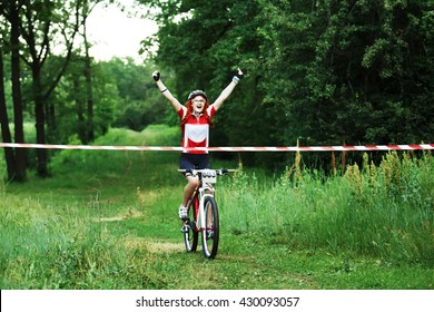 Winner Of Mtb Race. Victory Moment. Young Female Cyclist In Protective Helmet Crossing The Finish Line Breaking The Tape. Victory Triumph In Sportive Competition, Wins The Cycling Race. Bicycle Sport.