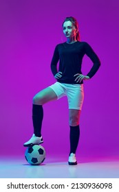 Winner. Portrait Of Beautiful Girl, Female Soccer Player With Football Ball Isolated On Purple Background In Neon. Concept Of Sport, Fitness. Young Spotive Girl In Black And White Football Kit