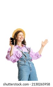 Winner. Studio Shot Of Young Happy Girl, Female Gardener In Work Uniform And Hat Using Phone Isolated On White Background. Concept Of Job, Wow Emotions, Agronomy. Funny Meme Emotions.