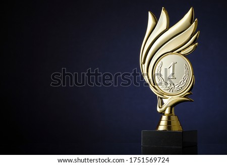 Winners gold trophy with engraved medallion with number 1 and laurel wreath surrounded by a swirl over a dark blue background with copyspace for a championship or competition