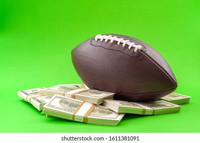 Winning Bet On Sporting Event, Money In Sport And Sports Betting Conceptual Idea With American Football Ball And Wads Of Cash Isolated On Green Background