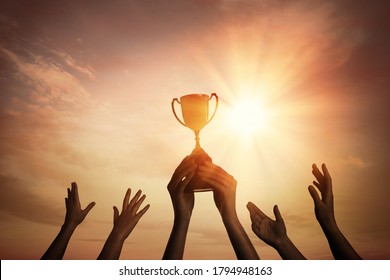 Winning team with gold trophy cup against shining sun in sky 