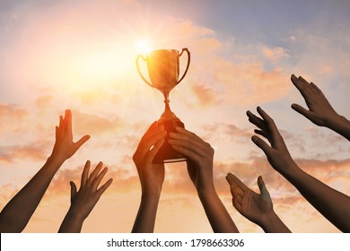 Winning team with gold trophy cup against shining sun in sky  - Shutterstock ID 1798663306