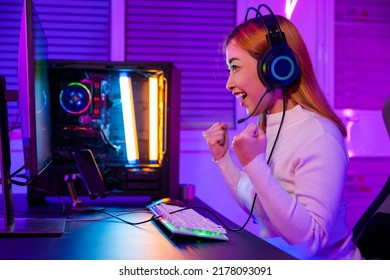 Winning Victory. Asian gamer playing online video game excited on desktop computer PC colorful neon LED lights, woman in gaming headphones use computer she happy successful, E-Sport concept, side view