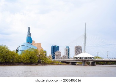 Winnipeg, Manitoba - June 12th 2020: The Assiniboine River Runs by the famous Skyline with the Canadian Human Rights Museum, the Downtown TD Building, and DisEsplanade Riel Footbridge