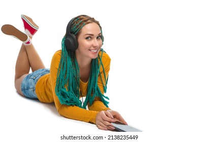 Winsome Positive Caucasian Female with African American Dreadlocks Listens Music in Wirreless Headphones Smartphone While Laying on Floor Over White. Horizontal Image Orientation