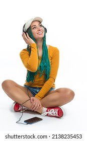 Winsome Positive Caucasian Female with African American Dreadlocks Listens Music in Wirreless Headphones Smartphone While Posing in Streetwear Clothing Over White. Vertical image Orientation