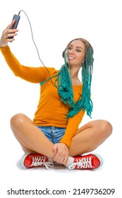 Winsome Positive Caucasian Female with African American Dreadlocks Taking Selfie With Cellphone While Listens Music in Wirreless Headphones Sitting on Floor Over White. Vertical image Orientation