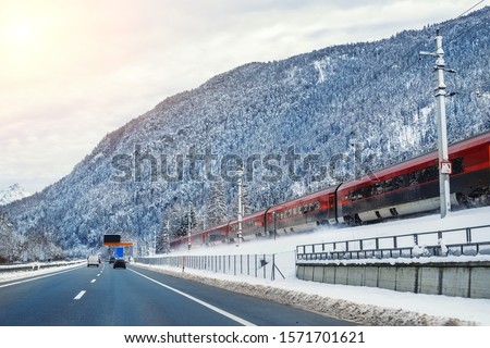Winter alpine mountain highway and parallel railway road with intercity fast train and blue sky on background at bright cold sunny day. Car trip family travel journey vacation. Transportation mode