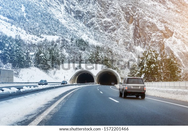 Winter alpine road landscape with tunnel,\
forest, mountains and blue sky on background at bright cold sunny\
day. Car trip family travel journey. Holiday skiing vacation.\
scenic austrian\
landscape