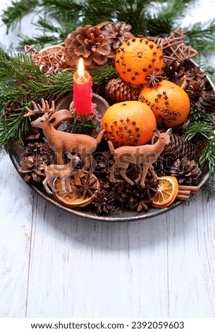 Winter altar for Yule sabbat. candle, toy deer family, cinnamon, nuts, cones, decorated oranges, fir branches in plate on wooden table. Christmas and new year concept. Festive winter season