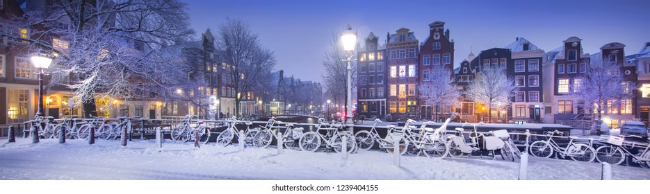 Winter in Amsterdam with snow. Panorama with bicycles, bridge, canal, old houses at night