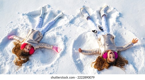 Winter Angels. Happy Kids Girls On Make Snow Angel Wings. Two Children Making Snow Angel, Lying On Snow. Excited Child Playing On Winter Background. Winter Games With Snow For Kids.