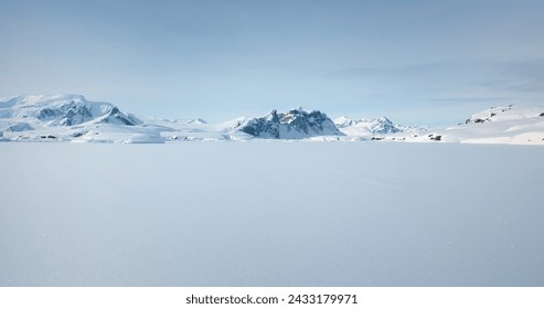 Winter Antarctica snow covered nature landscape. Frozen ocean, mountain range in background, sunny weather, blue sky. Desert white land of ice. Polar arctic travel scene. Low angle drone flight - Powered by Shutterstock