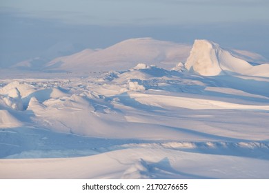 Winter arctic landscape. Ice hummocks on the frozen sea in the Arctic. Cold frosty winter weather. Harsh polar climate. View of snow-covered ice and snow-capped mountains. Amazing nature of the Arctic