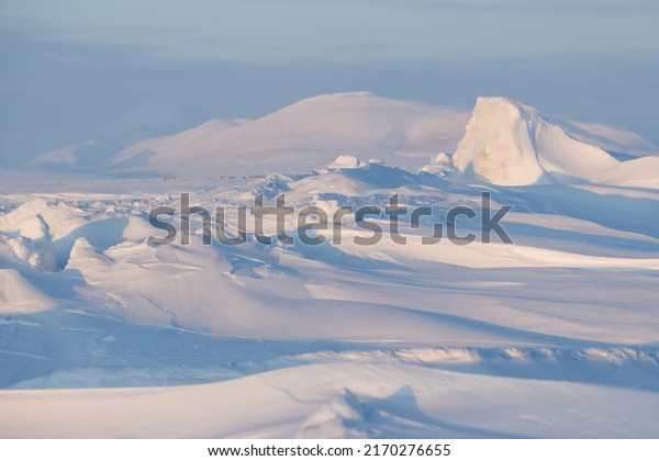 Winter arctic landscape. Ice hummocks on the\
frozen sea in the Arctic. Cold frosty winter weather. Harsh polar\
climate. View of snow-covered ice and snow-capped mountains.\
Amazing nature of the\
Arctic