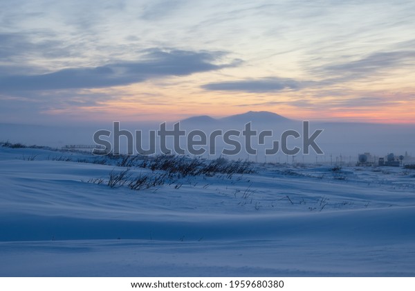 Winter arctic landscape. Polar twilight in the\
tundra. Cold frosty winter weather. Cold polar climate. In the\
distance, satellite dishes in the snowy tundra. Chukotka, Siberia,\
Far North of Russia.
